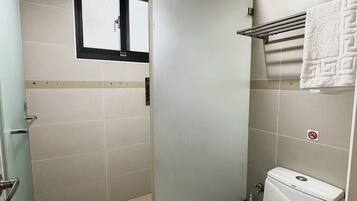 A small bathroom with a toilet, a shower stall, and a window.