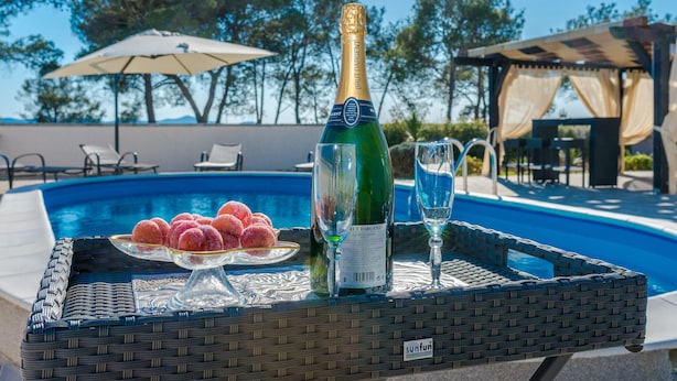 Une ambiance détendue au bord de la piscine, avec une bouteille de champagne, un verre et un plateau rempli de petites douceurs roses.