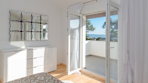 Une chambre avec une grande fenêtre, un lit, une commode et un miroir fixé au mur.