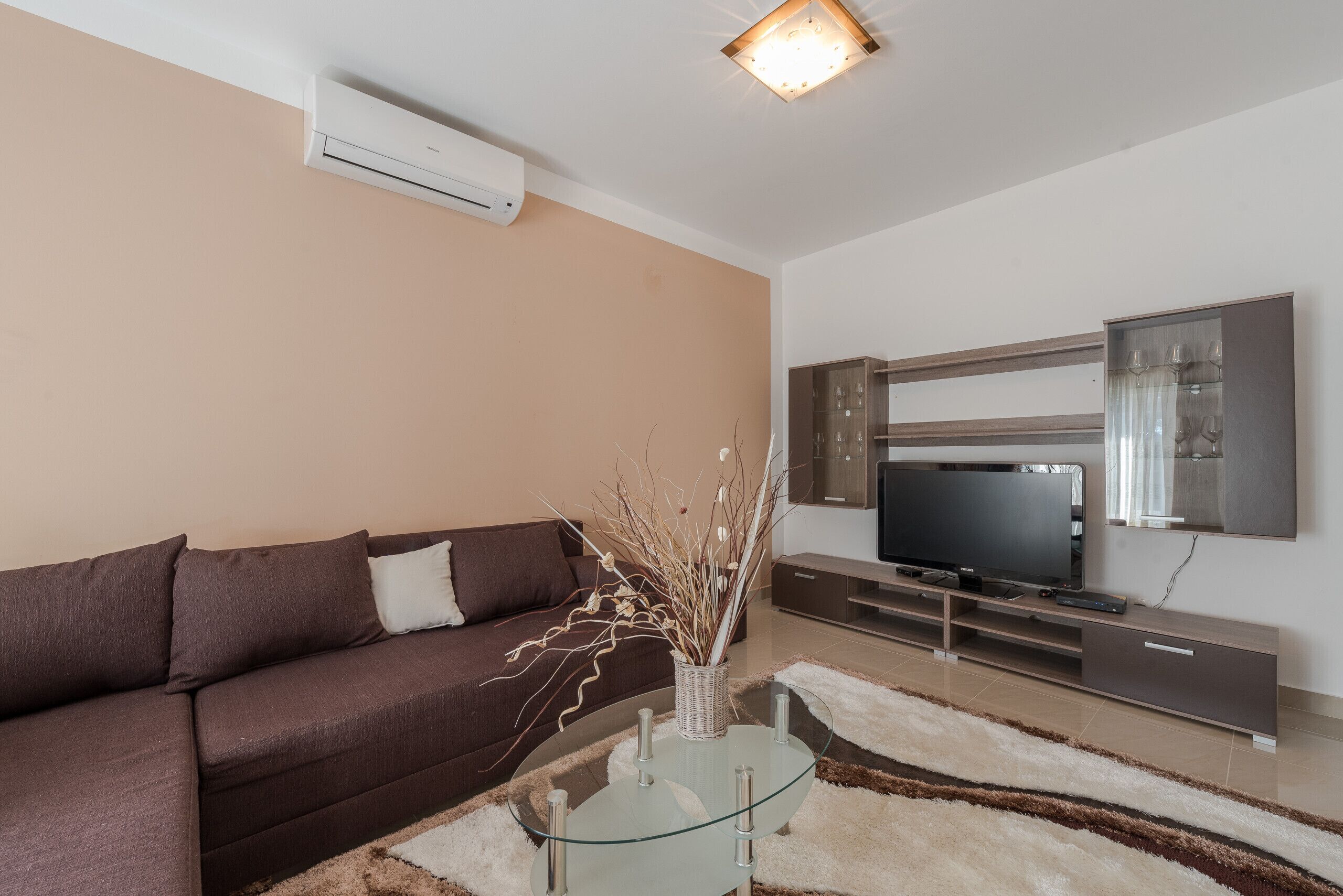 Una sala de estar moderna con un sofá marrón, una mesa de centro de vidrio, un televisor de pantalla plana y un mueble minimalista.