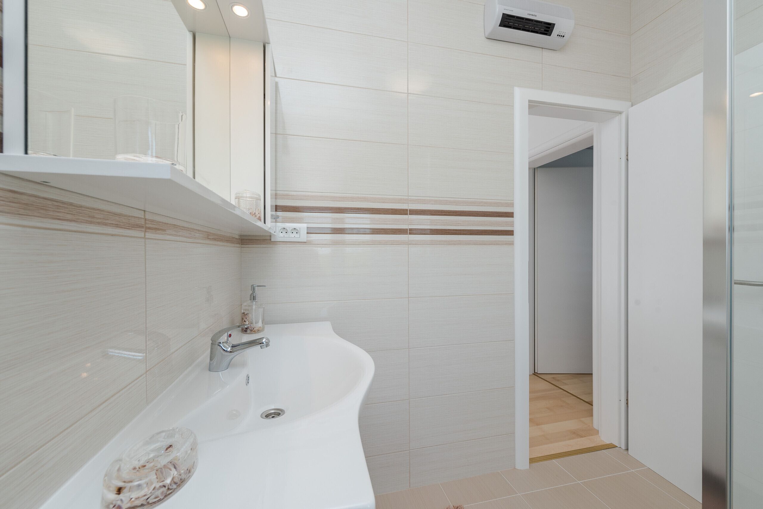 Une salle de bain moderne avec un lavabo blanc, un miroir et un espace douche.