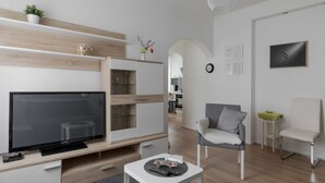 Ein modernes Wohnzimmer mit Flachbildfernseher, einer Couch, einem Couchtisch und einem Essbereich mit einer Glasvitrine.