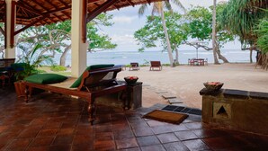 A covered outdoor seating area with a view of the ocean, wooden furniture, and tropical plants. - South Point Abbey Whole Villa 4 Bedroom (Sleeps 9) (Koggala)