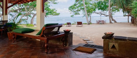 Un espace extérieur aménagé avec des sièges, abrité et offrant une vue sur l’océan, avec des meubles en bois et des plantes tropicales.