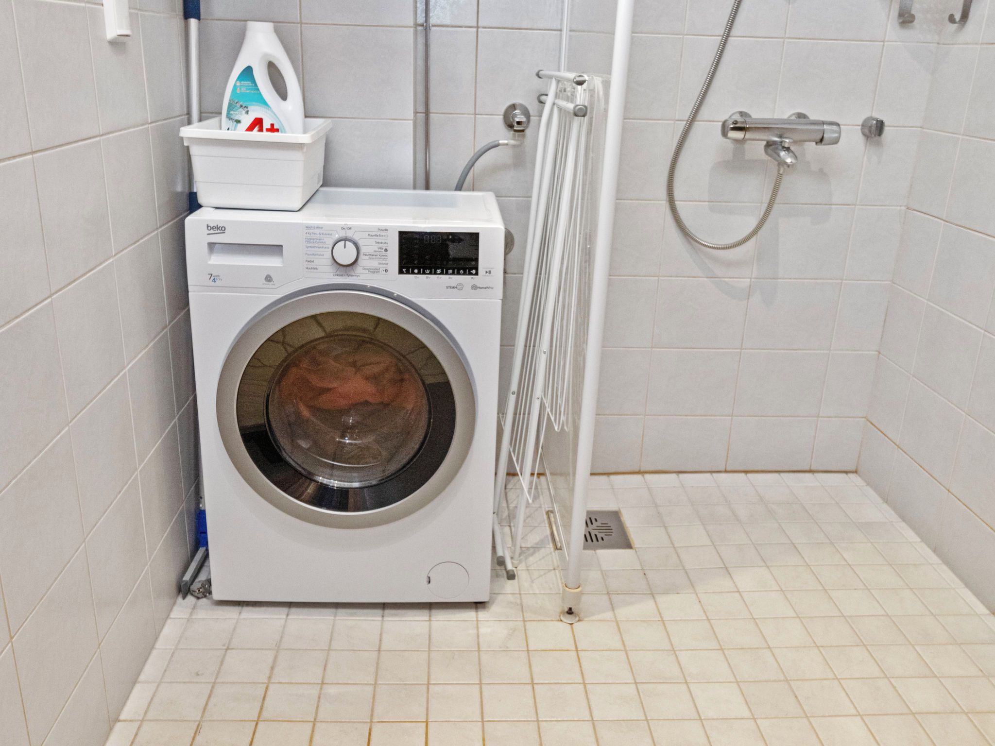 A compact washing machine in a small bathroom with a shower area.