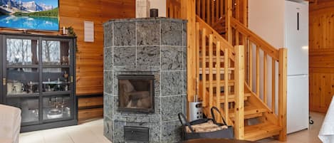 A wooden interior with a stone fireplace, a television, and a staircase.
