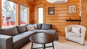 Ein gemütliches Blockhaus-Interieur mit einem grauen Ecksofa, einem runden Couchtisch und einem weißen Sessel.