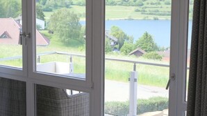 Quarto com uma janela grande com vista para um lago e vegetação.