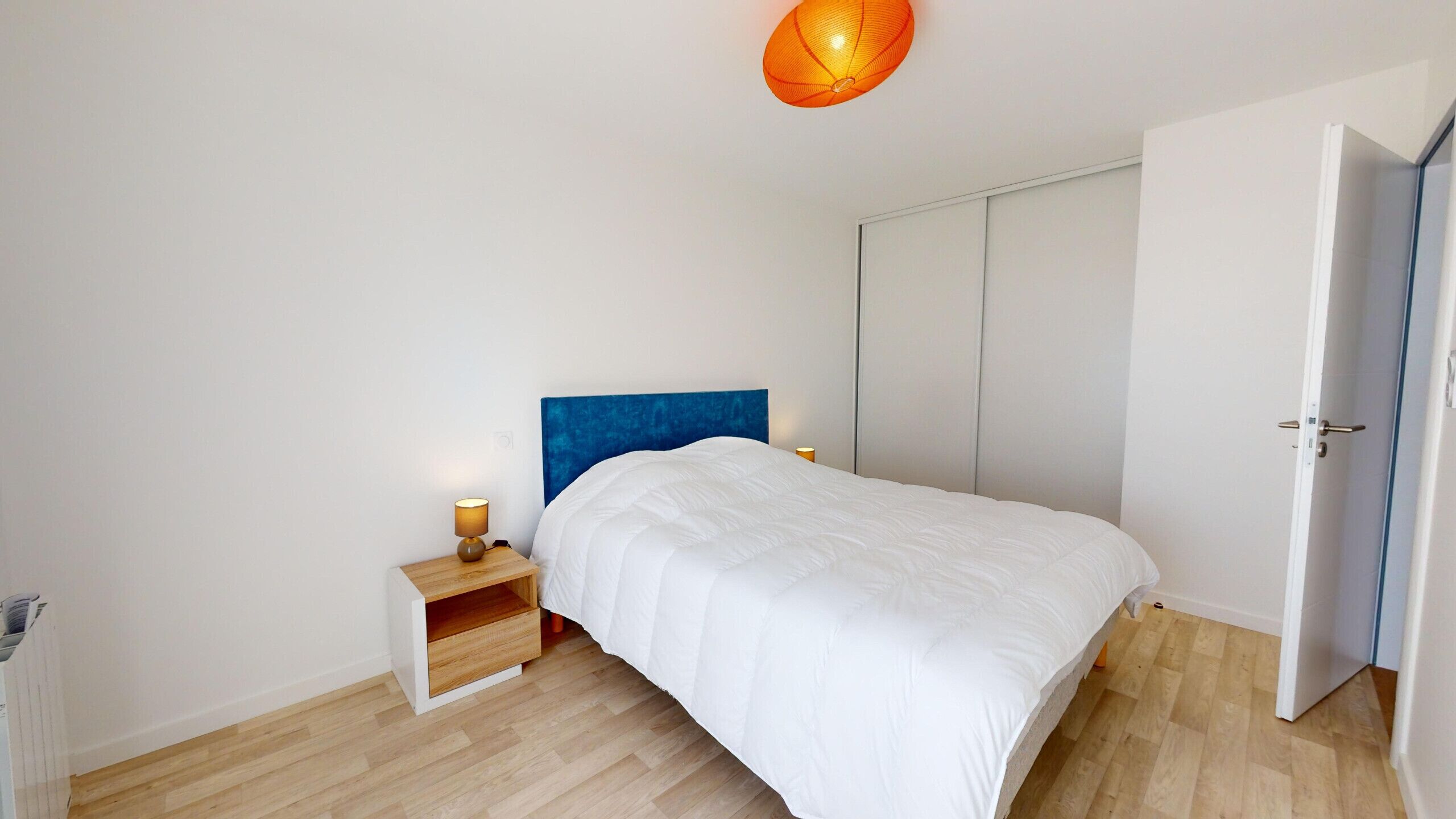 A bedroom with a bed, a nightstand, a wardrobe, and a hanging light fixture.