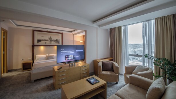 A hotel room with a bed, a TV displaying a Google homepage, a desk, a chair, and a large window with a view. - Putnik Inn Belgrade (Belgrade)