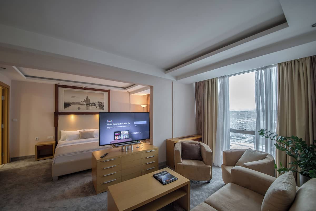 Ein Hotelzimmer mit Bett, Fernseher, der eine Google-Startseite anzeigt, Schreibtisch, Stuhl und einem großen Fenster mit Blick.