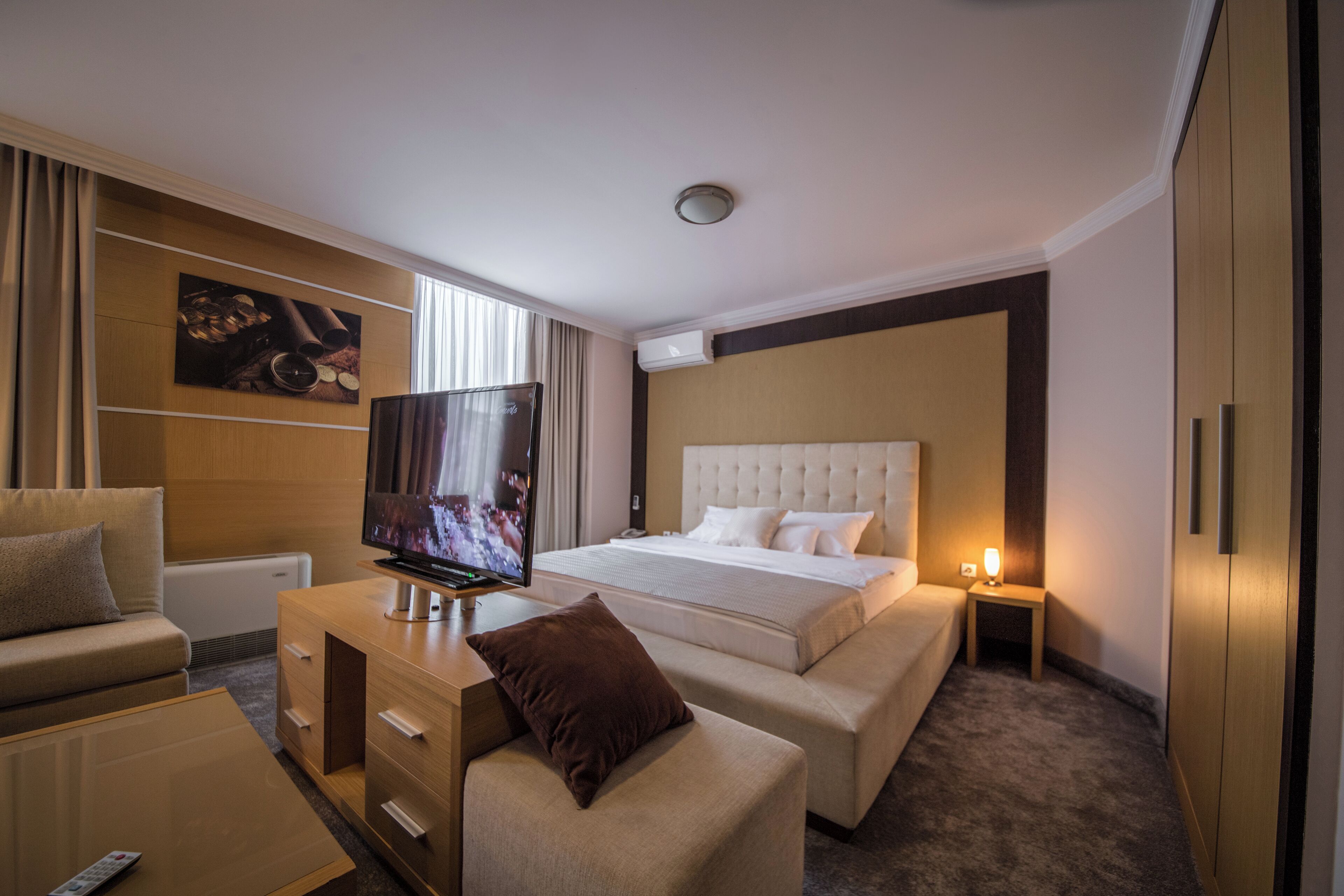Una habitación de hotel con una cama grande, televisión, sofá, escritorio y una mesita de noche con lámpara.