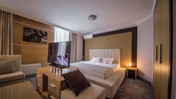 Una habitación de hotel con una cama grande, televisión, sofá, escritorio y una mesita de noche con lámpara.