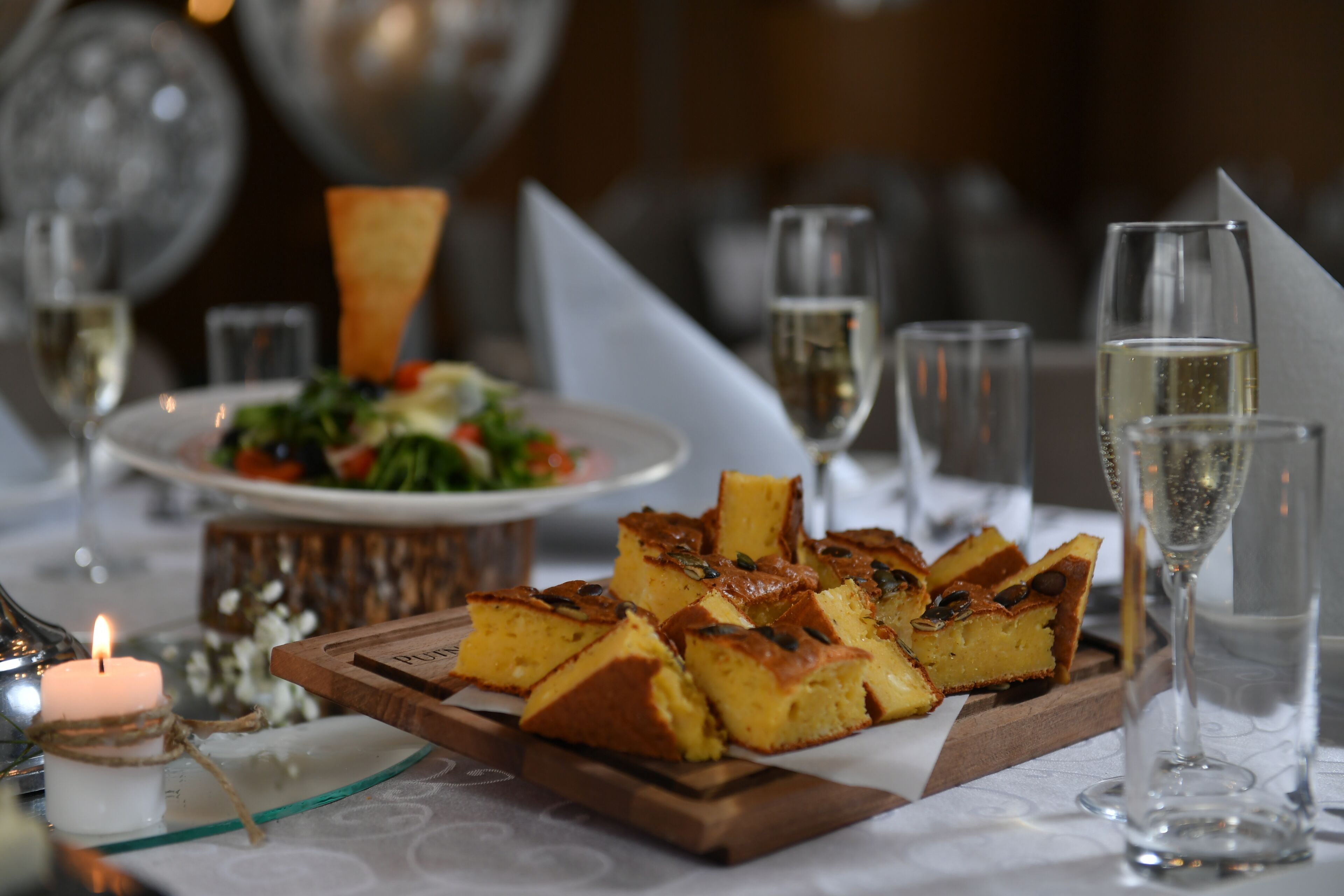 A table set with a wooden board of bread, glasses of champagne, and a lit candle.
