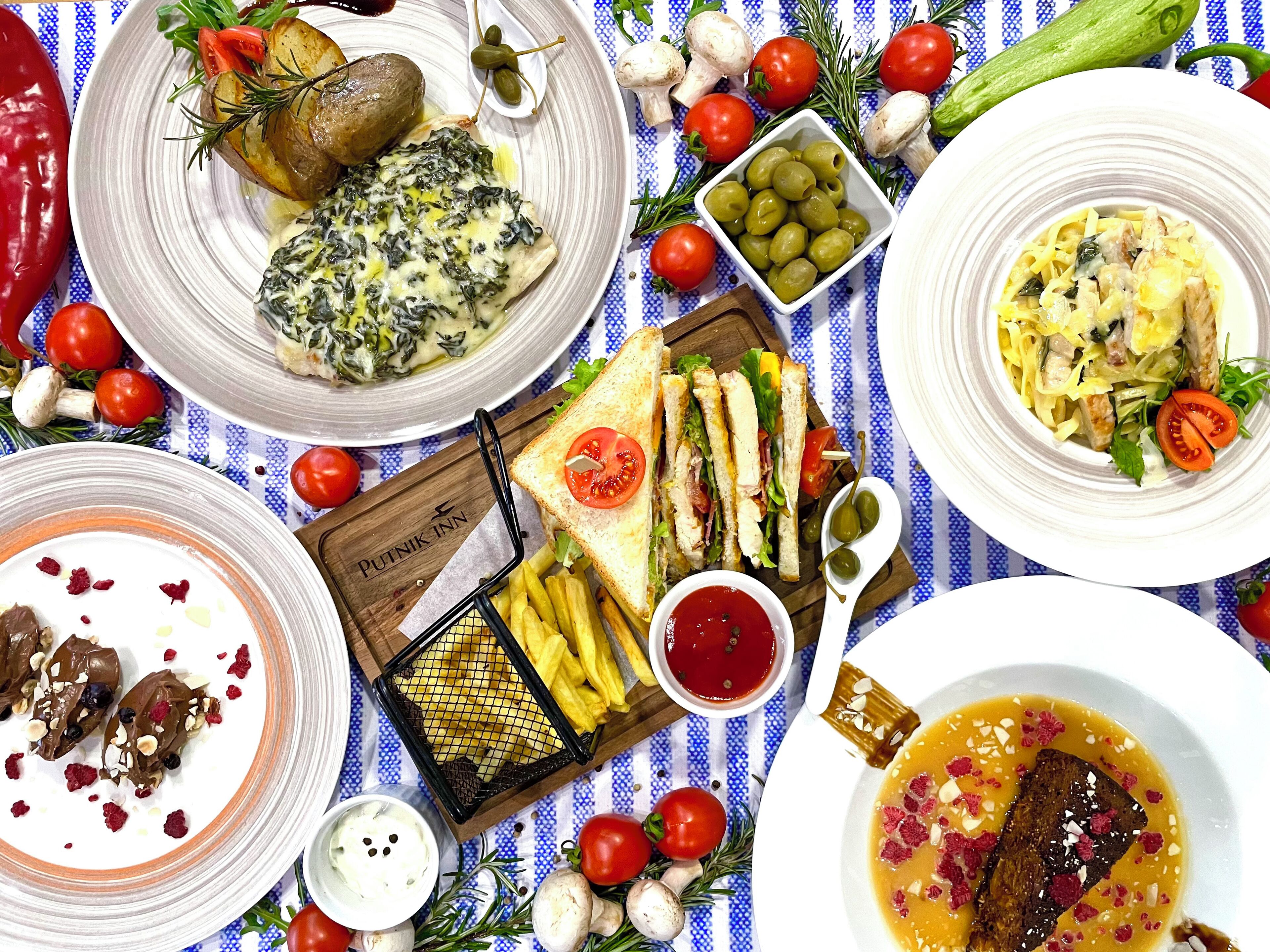Variedad de platos, incluyendo una porción de pasta, un sándwich y un tazón de sopa, todo sobre un mantel a rayas azules y blancas.