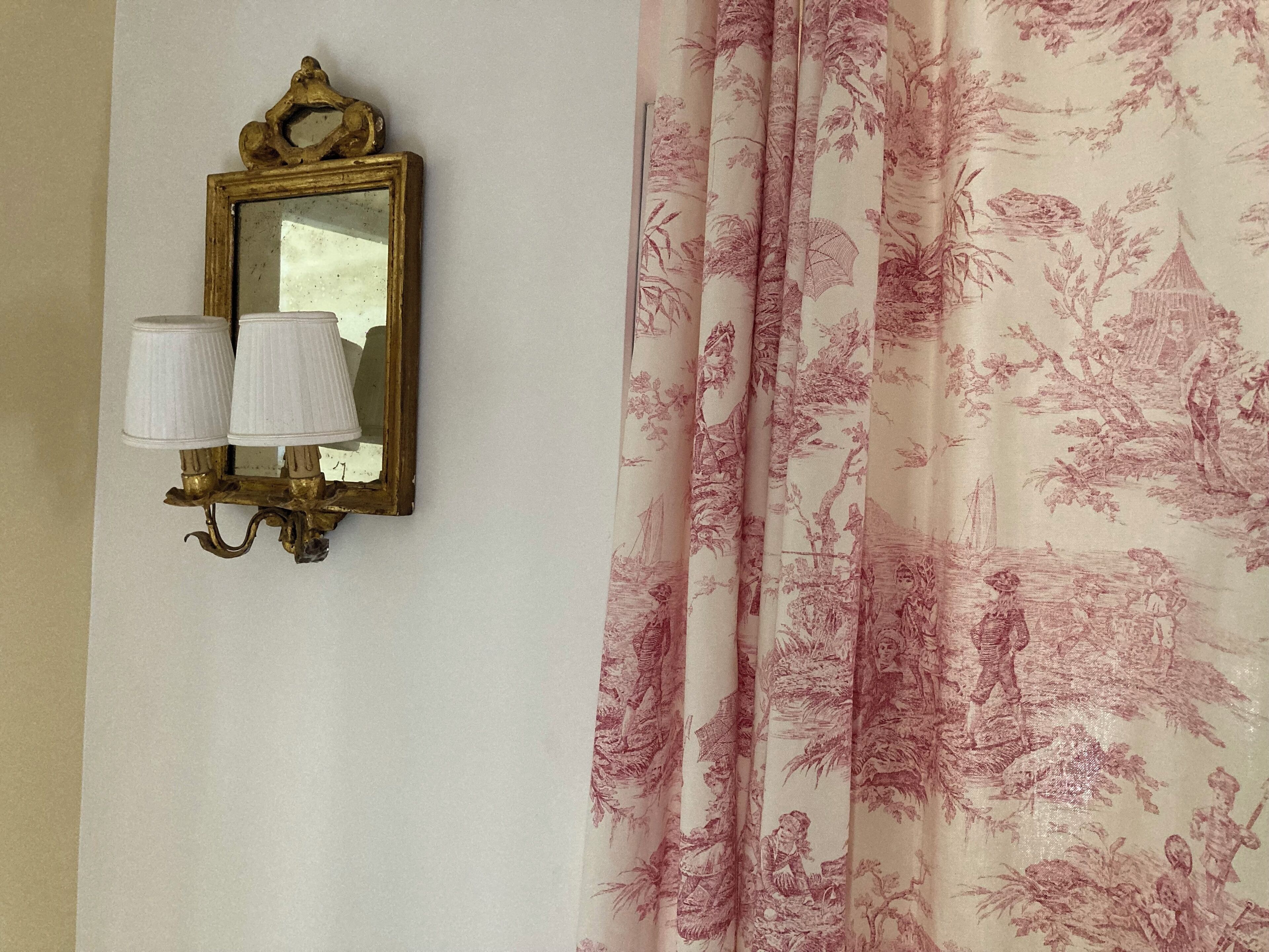 A wall-mounted mirror with two lamps and a floral-patterned curtain.