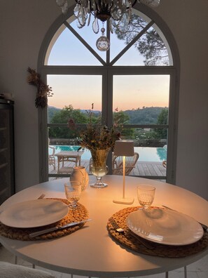 A dining table set for two with a view of a swimming pool and greenery outside. - Chic et Charme, Magnifique Bastide à Grasse 12 Personnes (Grasse)