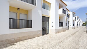 A row of modern, white buildings with balconies, a cobblestone street, and a clear sky.