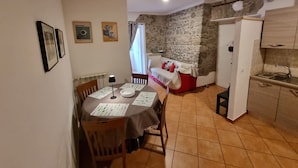 Uma sala de jantar com uma mesa posta para dois, um sofá vermelho, uma parede de pedra, uma cozinha com pia e um radiador.