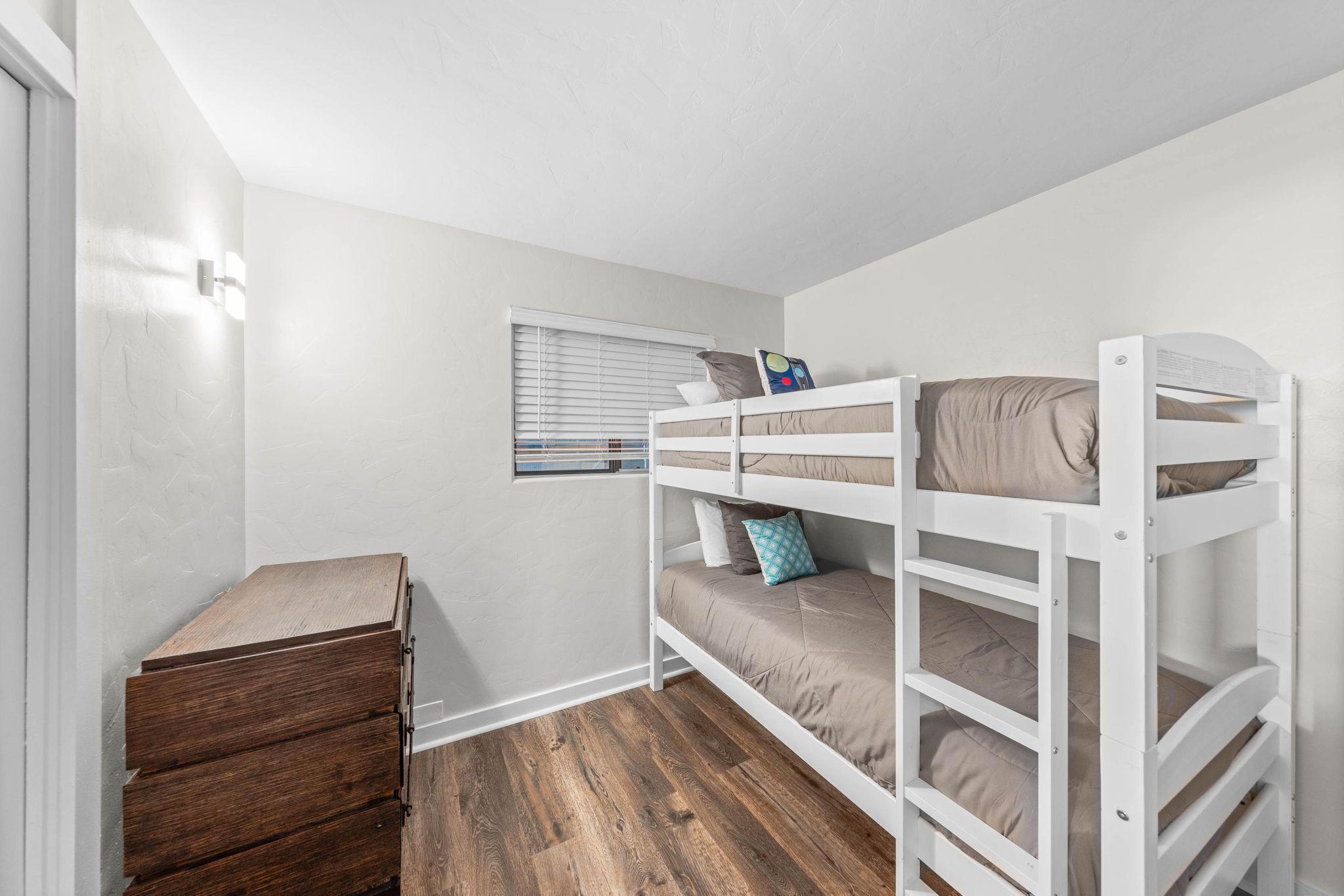 Habitación con literas, un aparador de madera, una ventana con persianas y techo blanco.
