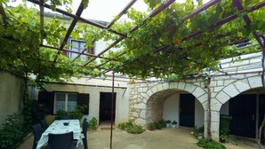 A covered patio with a table and chairs, stone arches, and a pergola with vines. - Holiday Home Katarina (Vinodol)