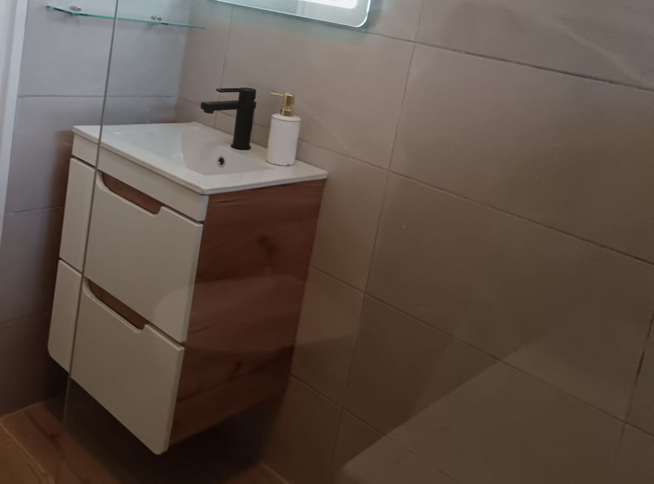 A small bathroom with a white sink, black faucet, and a glass shelf above it.