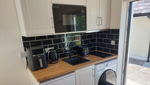 A compact kitchen with white cabinets, a black tiled backsplash, a built-in microwave, a kettle, a toaster, and a washing machine. - Studio | Sleeps 3 | Mountain Views - 5 Mins from Kenmare town. (Kenmare)