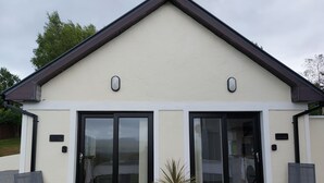 A modern building with a beige facade, large sliding glass doors, and a black roof. - Studio | Sleeps 3 | Mountain Views - 5 Mins from Kenmare town. (Kenmare)