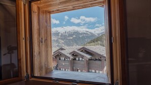 A wooden-framed window with a view of a mountain landscape and a building with multiple garage doors. - Studio Rénové à Grimentz (Grimentz)
