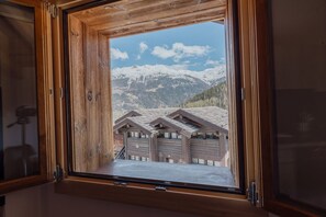 Ventana de madera con vistas a un paisaje montañoso y un edificio con varias puertas de garaje.