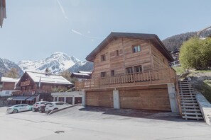 Un chalet de madera con balcón, garaje y zona de aparcamiento con coches.