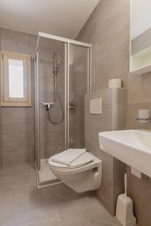 Un baño moderno con ducha de vidrio, inodoro blanco y lavamanos con espejo.