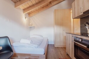 Une chambre à coucher comprenant un lit, une chaise, un plafond en bois et un coin cuisine avec des placards et des appareils électroménagers.
