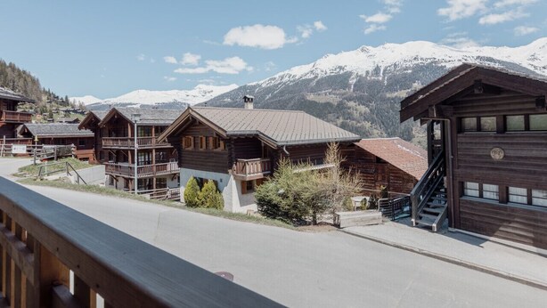 Une rangée de chalets en bois dotés de balcons, se dressant sur fond de montagnes enneigées.
