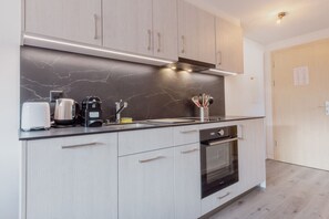 Une cuisine moderne avec des meubles en bois clair, un pare-feu en marbre et des appareils électroménagers en acier inoxydable, notamment une machine à café, un grille-pain et un four.