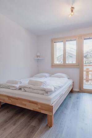 Un dormitorio con una cama de madera, una ventana con vistas y una lámpara fijada a la pared.