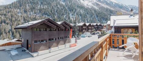 Ein Holzhaus mit Balkon, Bergkulisse und blauem Himmel.