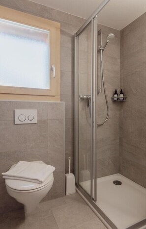 Un baño moderno con cabina de ducha de vidrio, inodoro y ventana sobre el lavabo.