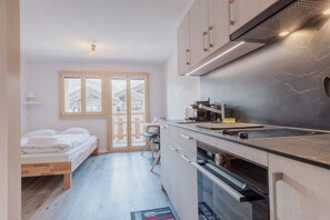 Cocina compacta con horno integrado, microondas y estufa a gas. Cuenta con un pequeño comedor con una silla y una mesa.