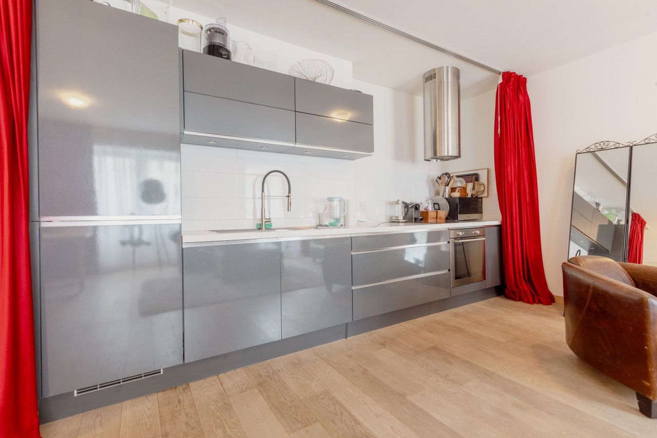 A modern kitchen with grey cabinets, stainless steel appliances, and a red curtain.