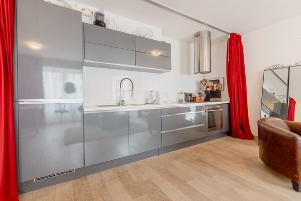 A modern kitchen with grey cabinets, stainless steel appliances, and a red curtain.