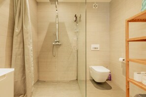 A modern bathroom with a glass shower enclosure, a white toilet, and a wooden shelf with toiletries.