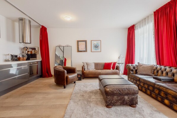 A modern living room with a sofa, ottoman, and a dining area with a kitchen counter.