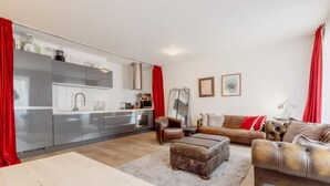A modern kitchen with stainless steel appliances, a dining area with a table and chairs, and a living room with a sofa and ottoman.