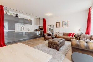 Una cocina moderna con electrodomésticos de acero inoxidable, un comedor con mesa y sillas, y una sala de estar con sofá y reposapiés.