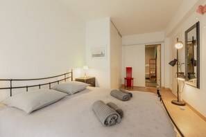 A hotel room with a bed, a nightstand, a lamp, a mirror, and a red chair.