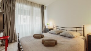 A bedroom with a bed, pillows, a bedside table, a lamp, and a bench.