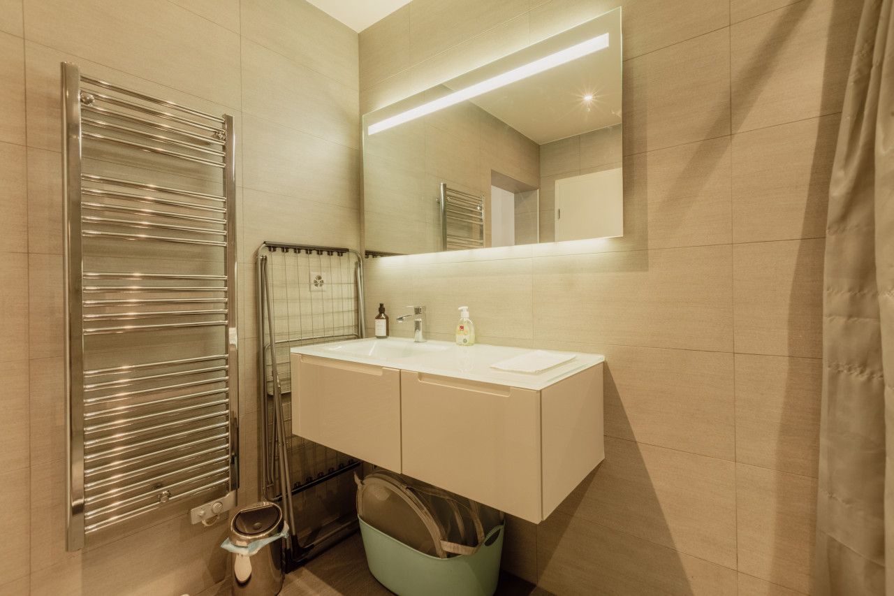 A modern bathroom with a double sink, a mirror, a towel rack, and a shower.