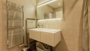 A modern bathroom with a double sink, a mirror, a towel rack, and a shower.