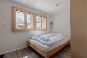 A bedroom with a wooden bed, a window with a view of mountains, and a wall-mounted lamp.